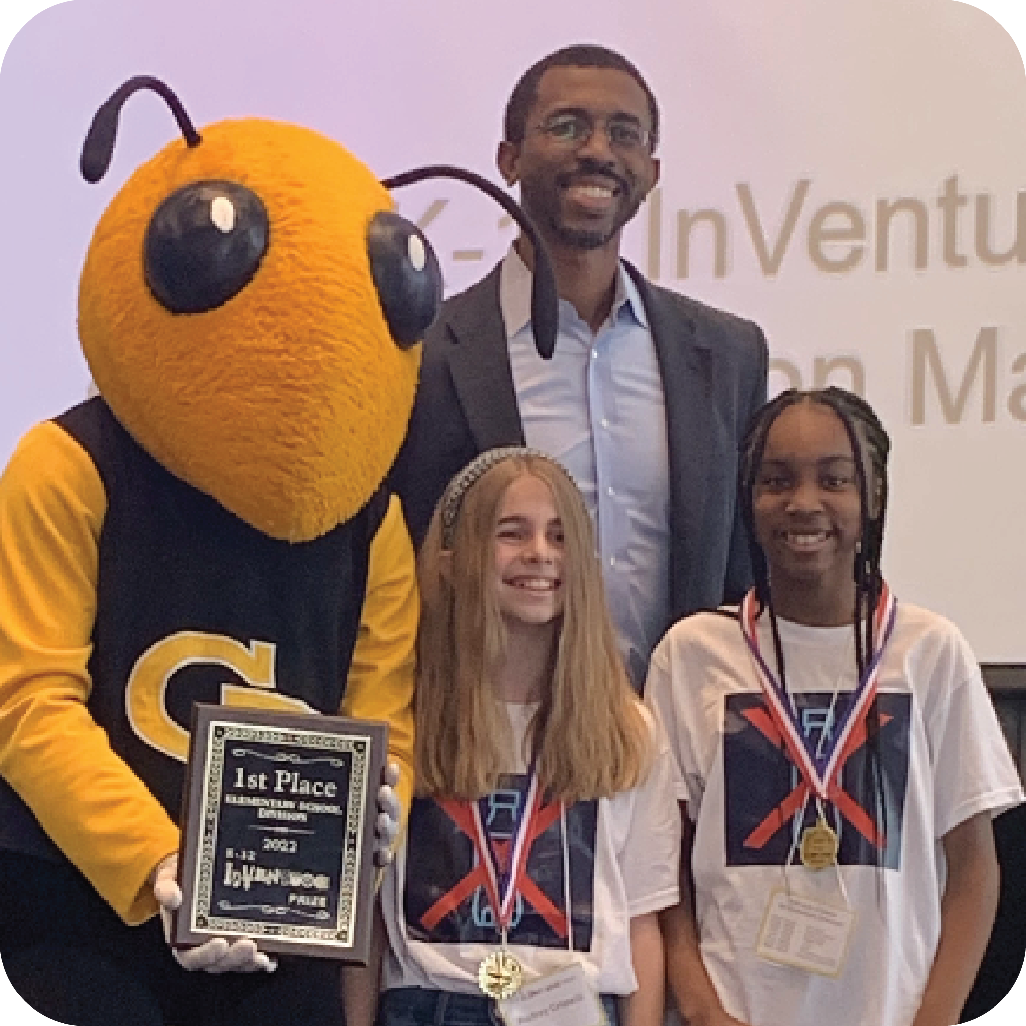Two smiling students standing next to Buzz (Georgia Tech's yellowjacket mascot)holding a plaque and Craig Cupid (Georgia Intellectual Property and Alliance representative).